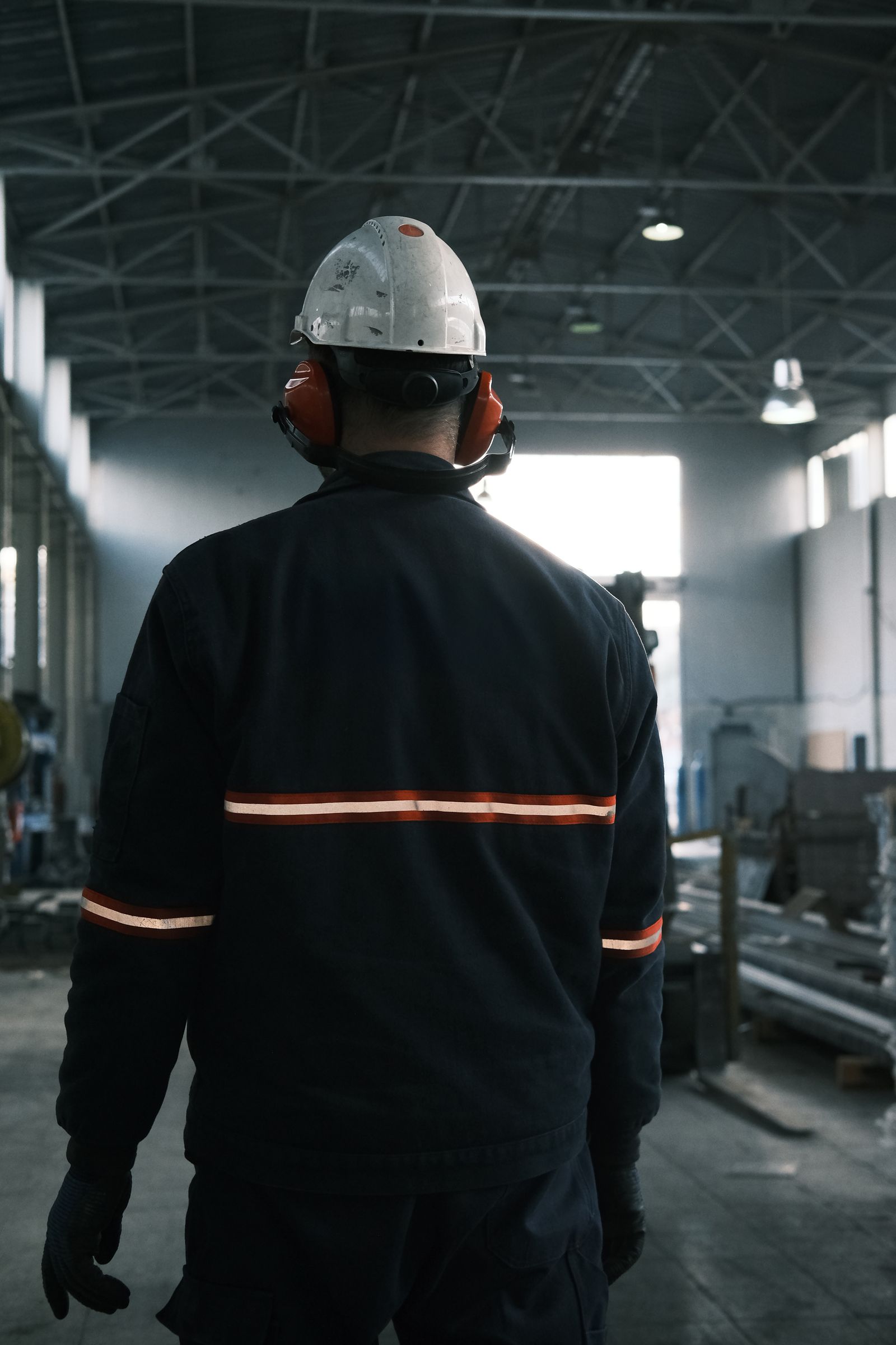 A worker in a hard hat and hearing protection walking through a plant floor